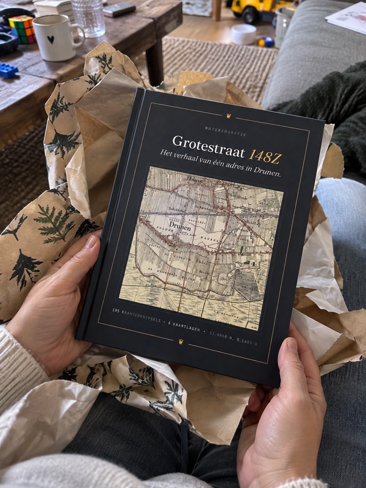 Twee handen pakken het gebonden boek uit vloeipapier, op schoot op de bank, met een koffiekop op de tafel ernaast