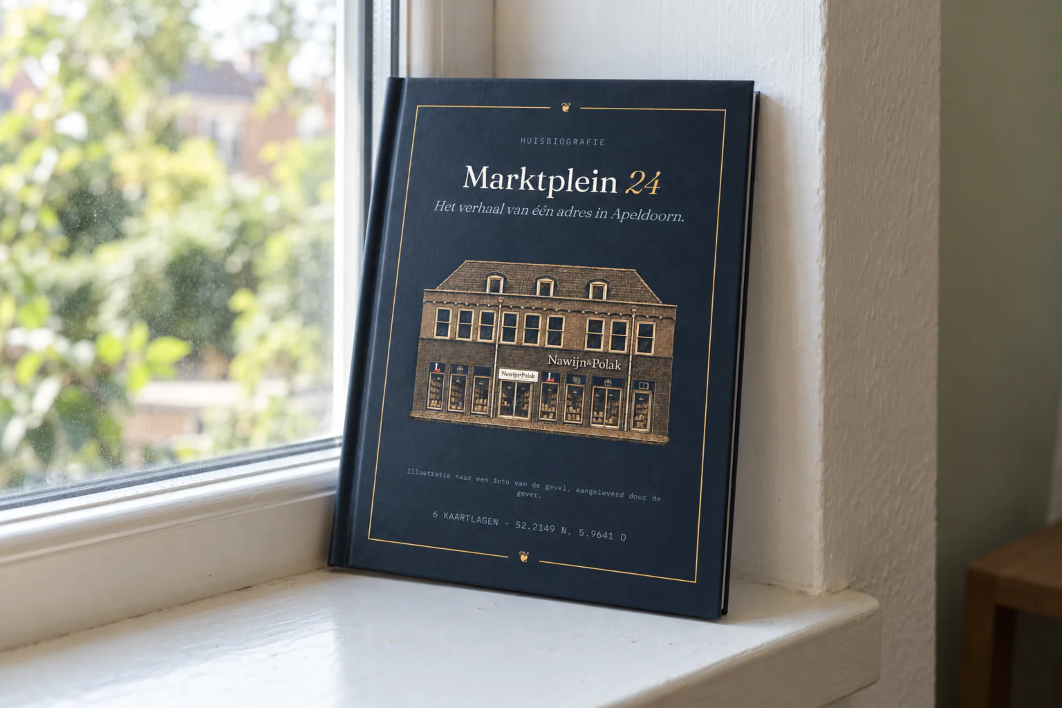 Het gebonden boek over Marktplein 24 in Apeldoorn staat rechtop in de vensterbank, tegen het raam; op de donkerblauwe kaft met gouden lijst staat een tekening van de gevel