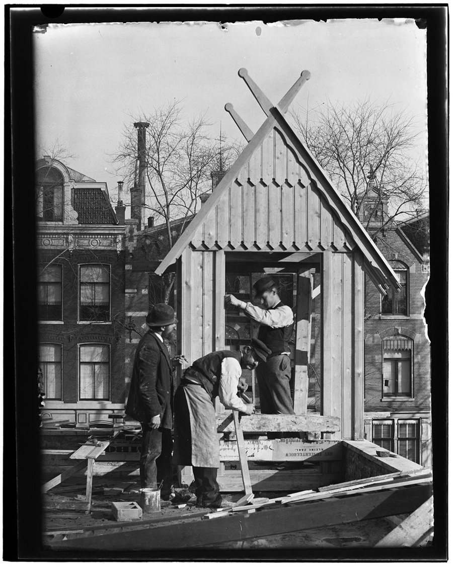 Zwart-witfoto van Amsterdamse bouwvakkers die rond 1890 aan een houten keet timmeren